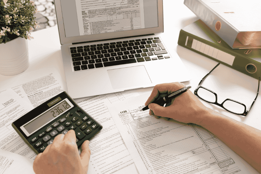 Person calculating finances with a calculator and tax forms, comparing APR and APY for loans and savings rates