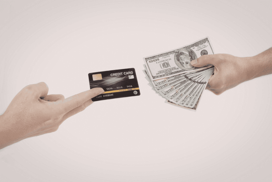Hand offering a credit card while another hand holds cash, illustrating credit card spending risk and repayment responsibility