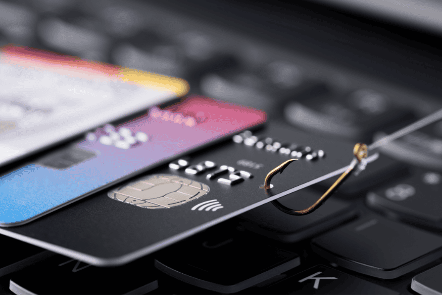 Credit cards hooked with fishing line on a keyboard, symbolizing phishing scams.