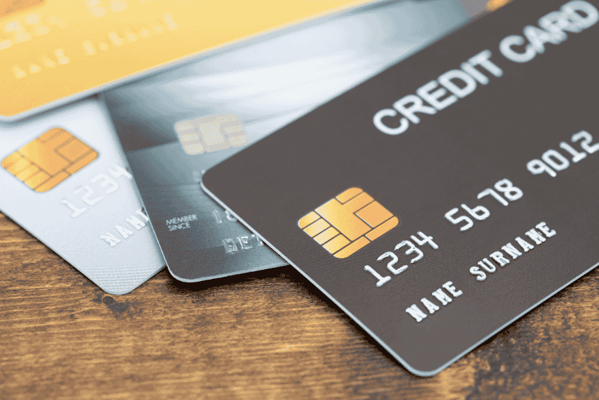 Stack of credit cards on wooden surface with visible chip and numbers