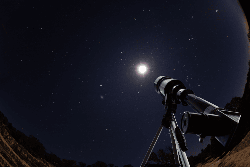 Telescópio apontado para a lua em céu noturno, com estrelas visíveis ao fundo.