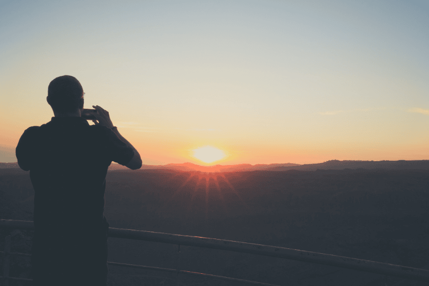 Pessoa fotografando o pôr do sol com o celular, preparando-se para registrar o céu noturno.