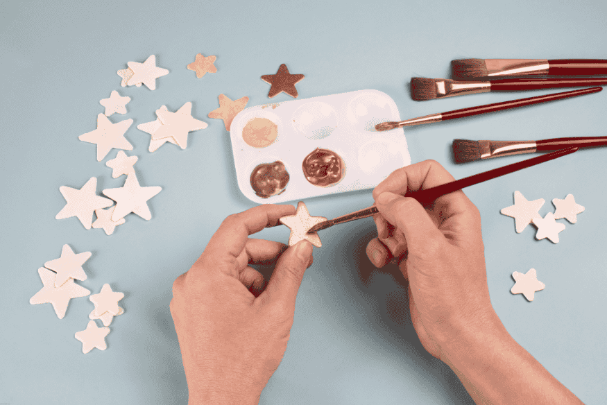Mãos humanas pintando estrelas em artesanato com tinta metálica