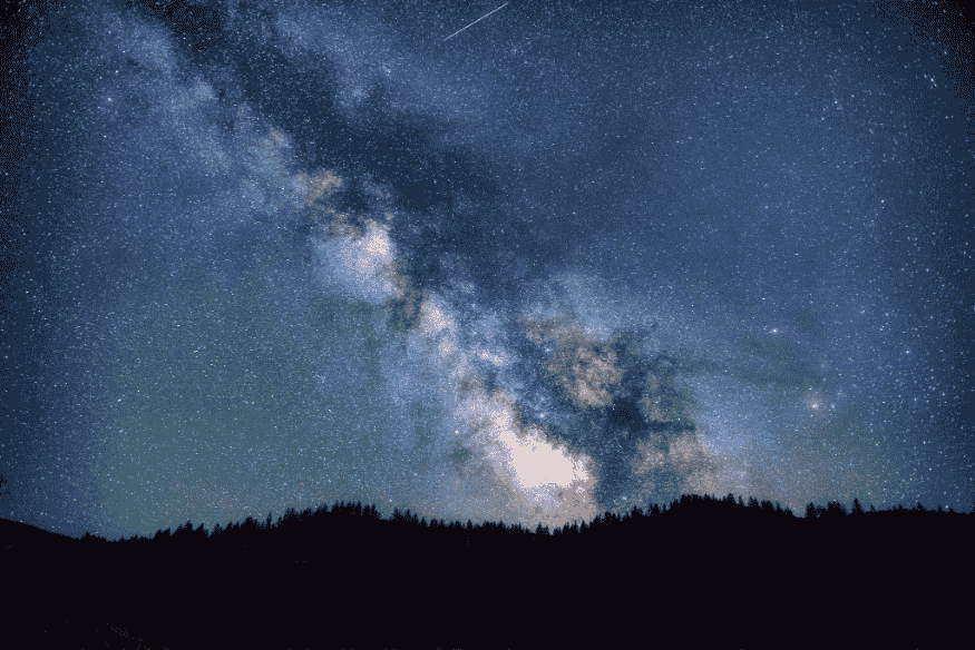 Céu noturno com a Via Láctea visível acima de uma linha de árvores