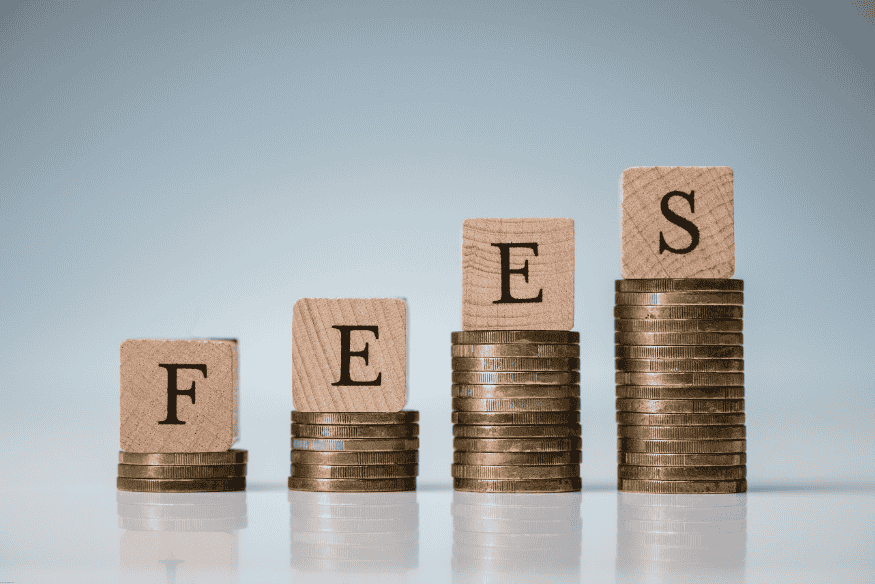 Wooden blocks spelling “FEES” placed on rising stacks of coins