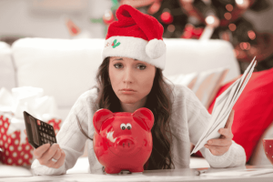 Woman in a Santa hat looking stressed with a calculator, bills, and a piggy bank during Christmas