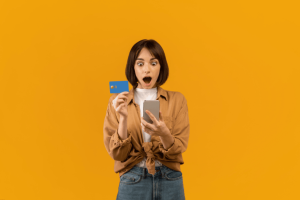 Excited woman holding a credit card and looking at her smartphone in surprise