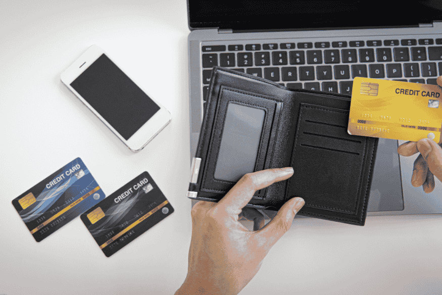 Person taking a yellow credit card from a wallet near a laptop and phone