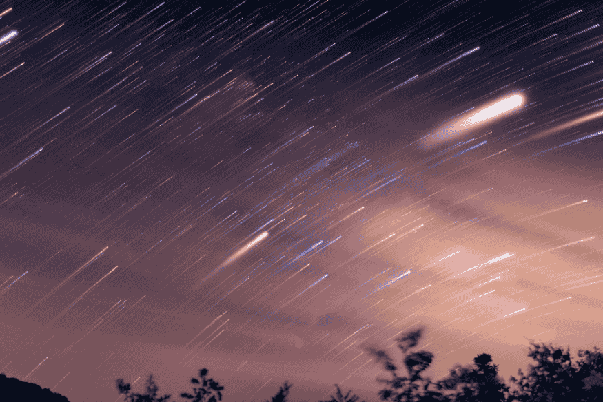 Rastreios luminosos no céu criados por meteoros e estrelas em longa exposição fotográfica.