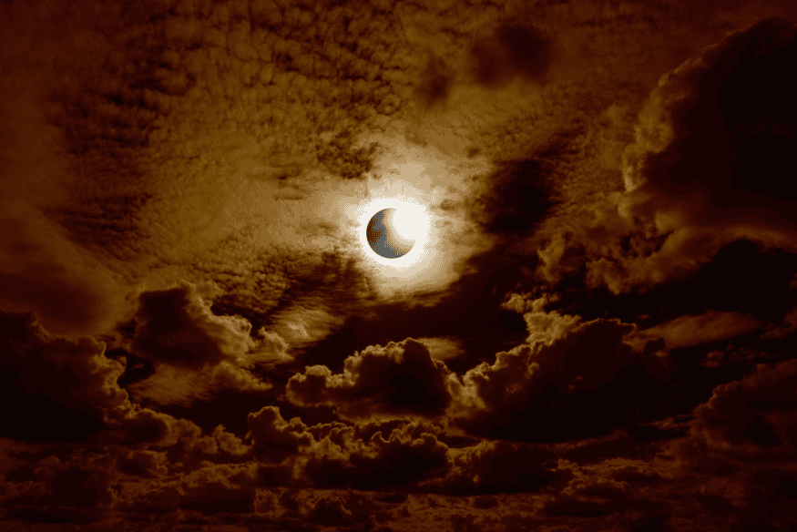 Eclipse solar parcial visto entre nuvens densas no céu noturno.
