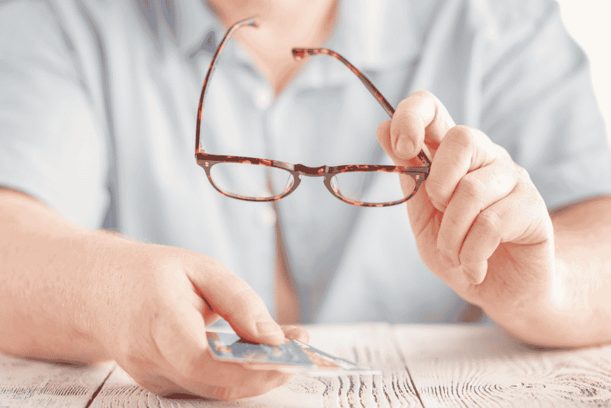 Person holding reading glasses and credit card at a table, reviewing fees
