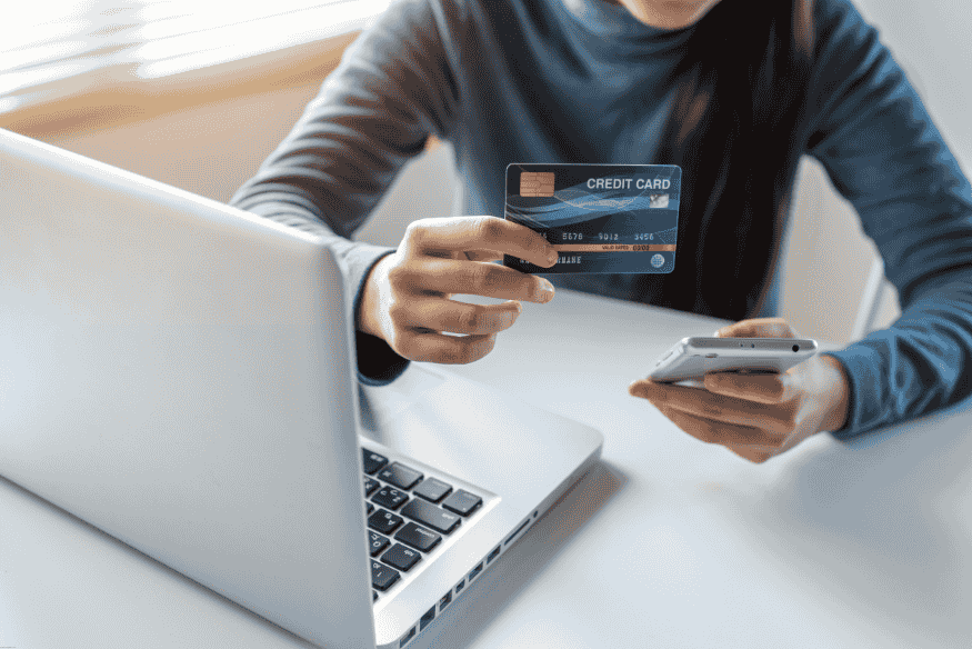 Woman holding a credit card and smartphone in front of a laptop.