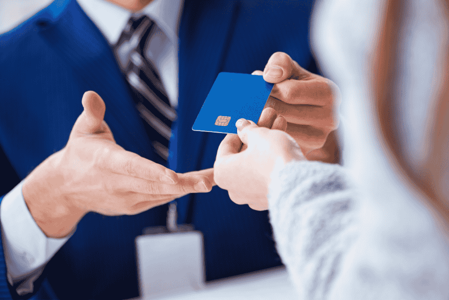 Person in a suit handing a blue credit card to a customer across a desk