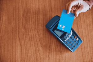 Hand tapping a blue contactless card on a payment terminal