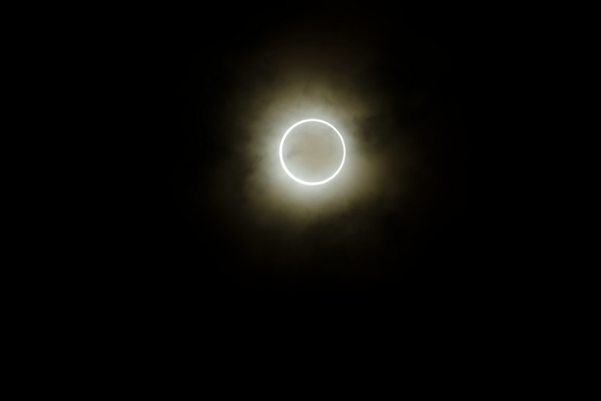 Eclipse anular visível por trás de nuvens, formando um anel de luz ao redor da Lua.