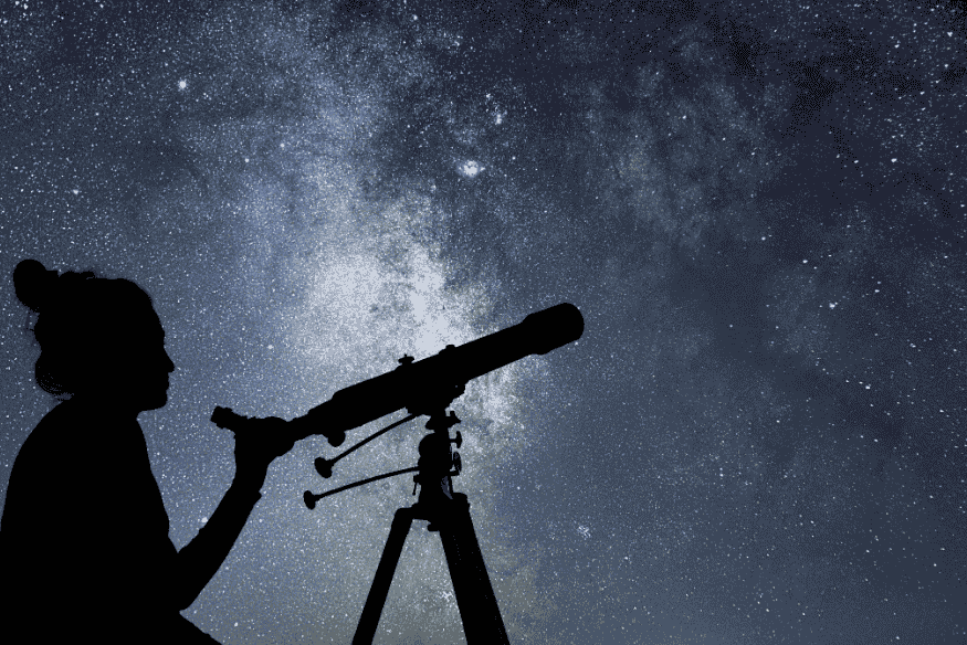 Pessoa ajusta telescópio com fundo de céu estrelado, preparando observação noturna.