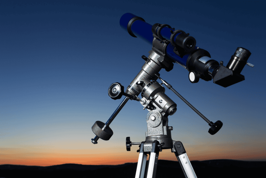 Telescópio com montagem equatorial apontado para o céu ao entardecer.