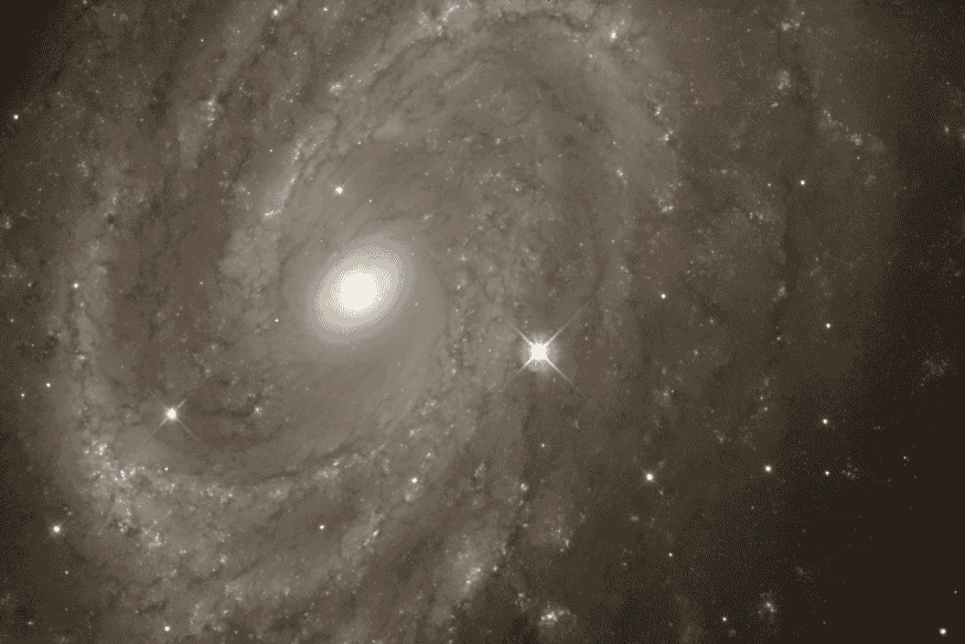 Galáxia espiral com núcleo brilhante e estrela variável destacada na imagem em alta resolução.