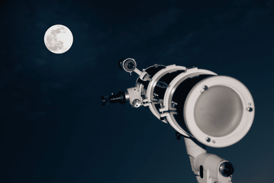 Telescópio apontado para a Lua cheia durante evento de observação noturna.