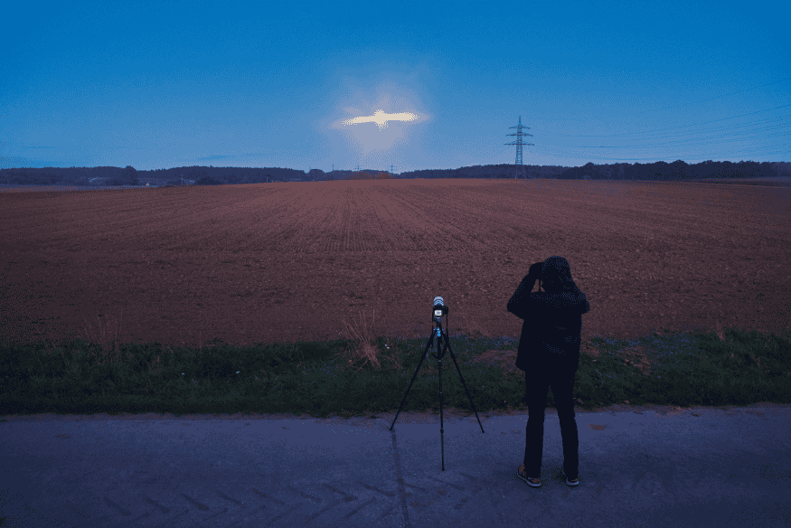 Fotógrafo em campo aberto com tripé, capturando a Lua nascendo no horizonte ao anoitecer.
