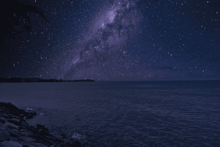 Via Láctea visível sobre o oceano à noite, ideal para astrofotografia com paisagem costeira.
