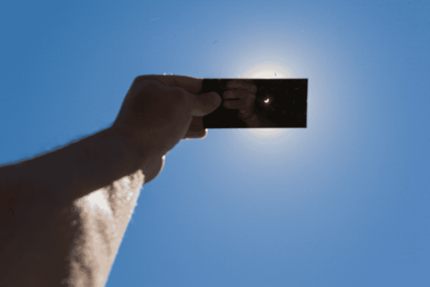 Pessoa segura protetor escurecido para observar eclipse solar com segurança durante o dia.
