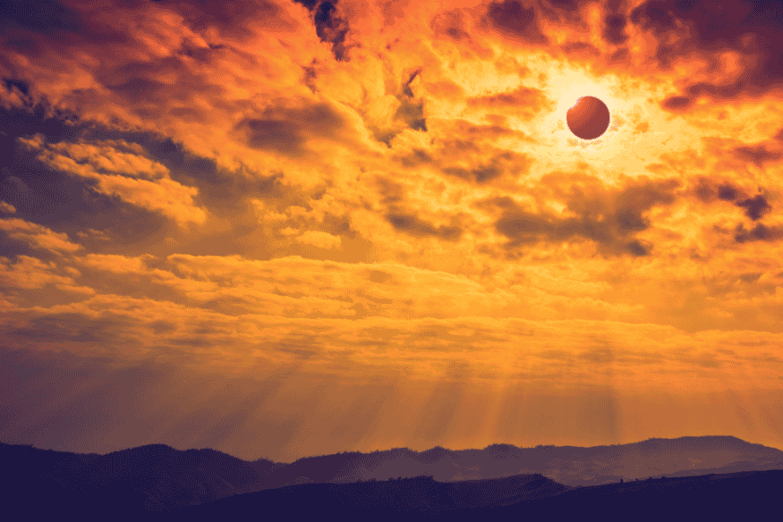 Eclipse solar visível entre nuvens laranja durante o entardecer em região montanhosa.