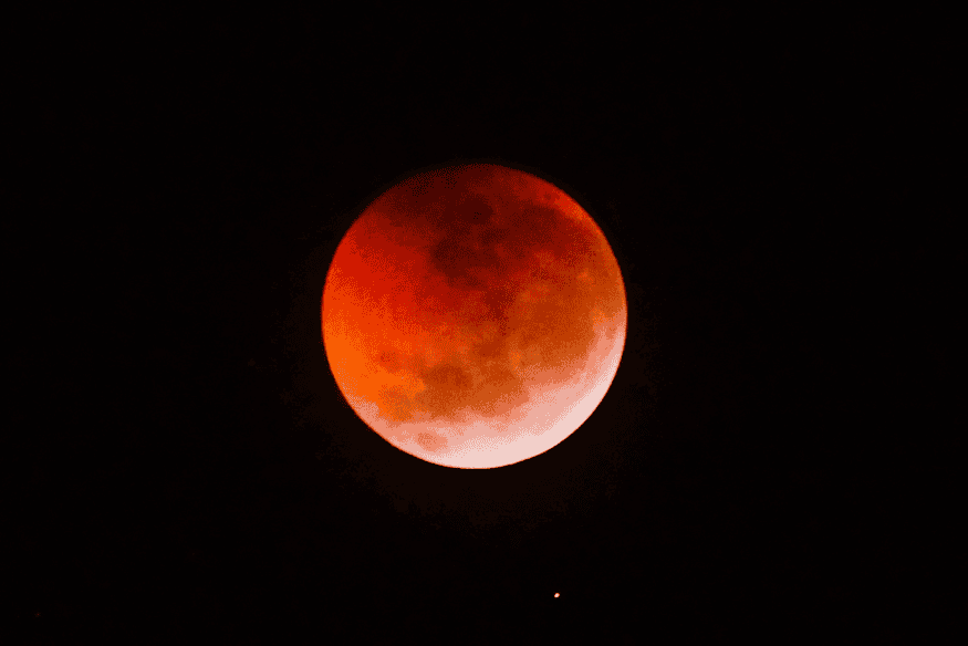 Lua durante eclipse lunar parcial com tons avermelhados visíveis no céu noturno.