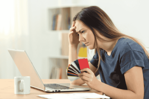 Woman looking worried at a laptop while holding multiple credit cards
