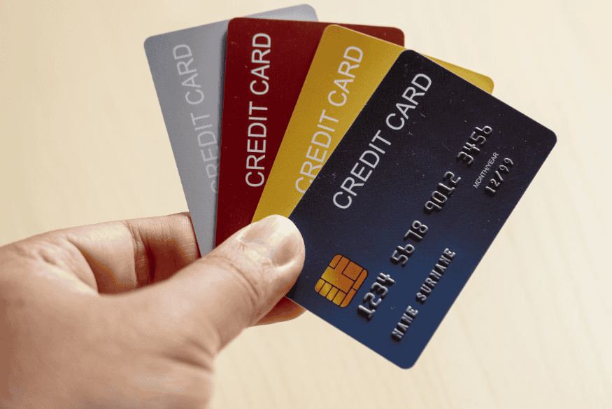 Hand holding four different colored credit cards spread out on a table