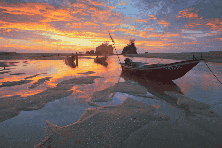 Barcos de pesca encalhados na areia durante a maré baixa ao pôr do sol.