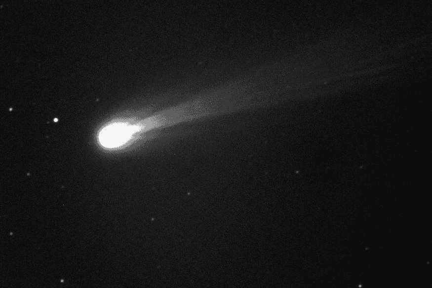 Cometa brilhando no céu noturno com rastro visível em direção diagonal.