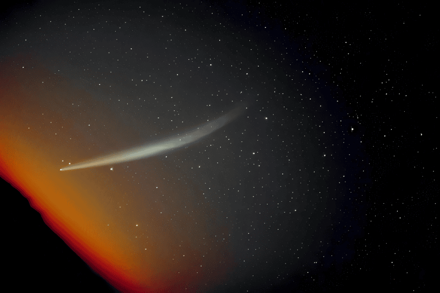 Cometa atravessando o céu entre estrelas, com brilho alaranjado próximo ao horizonte.