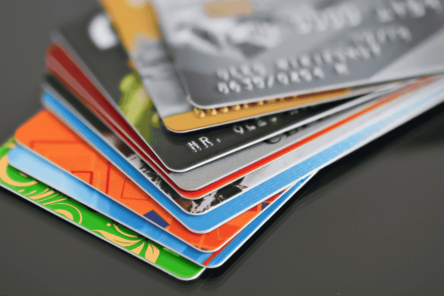 Stack of various colorful credit cards placed on a glossy black surface.