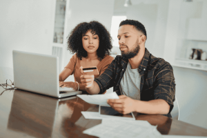 Couple managing credit card payments together at home using a laptop and paper statements.