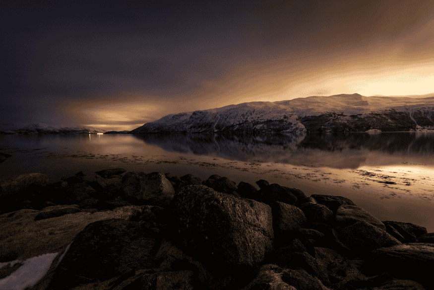 Reflexo da poluição luminosa sobre montanhas nevadas e lago durante a noite.