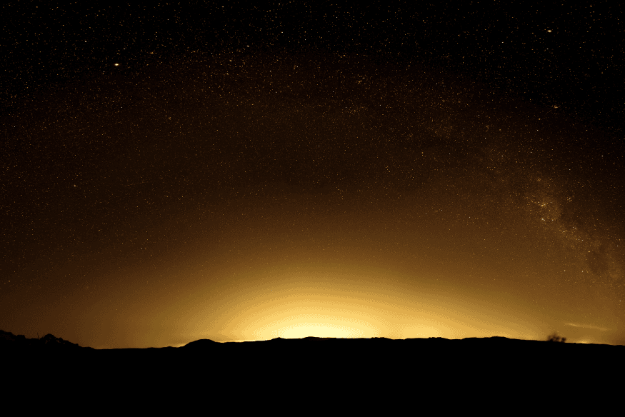 Céu noturno encoberto por poluição luminosa intensa, com estrelas ofuscadas no horizonte.