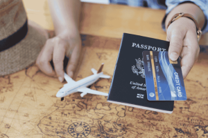Person holding a credit card and a passport with a toy airplane on a map background