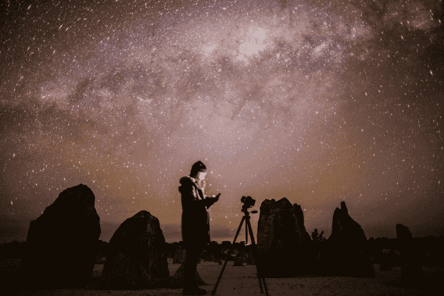 Fotógrafo ajustando câmera para capturar a Via Láctea em destino de observação astronômica.