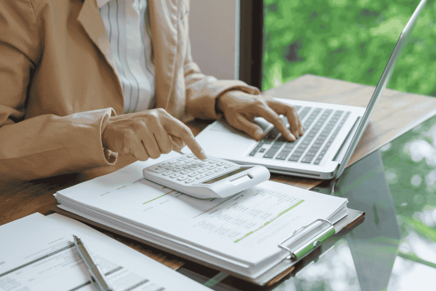 Person calculating expenses on a laptop and calculator while reviewing paperwork to set up automatic savings