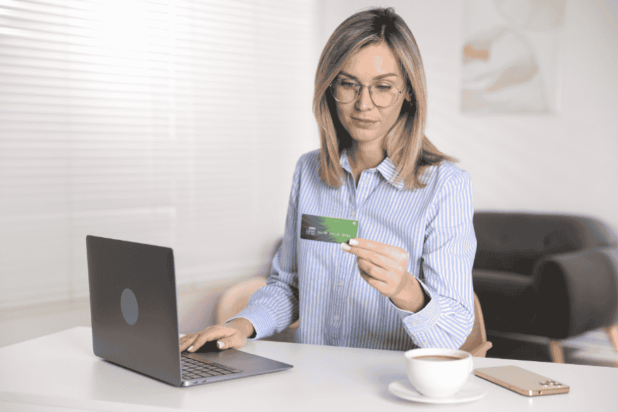 Woman holding a credit card next to a laptop, reviewing balance transfer terms and fees online
