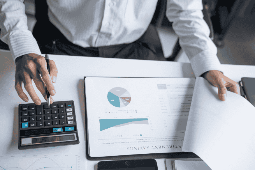 Person using a calculator and reviewing financial reports, illustrating how to calculate net worth from assets and liabilities