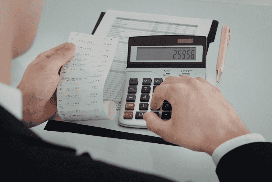 Person using a calculator while checking receipts and a ledger during a weekly expense review