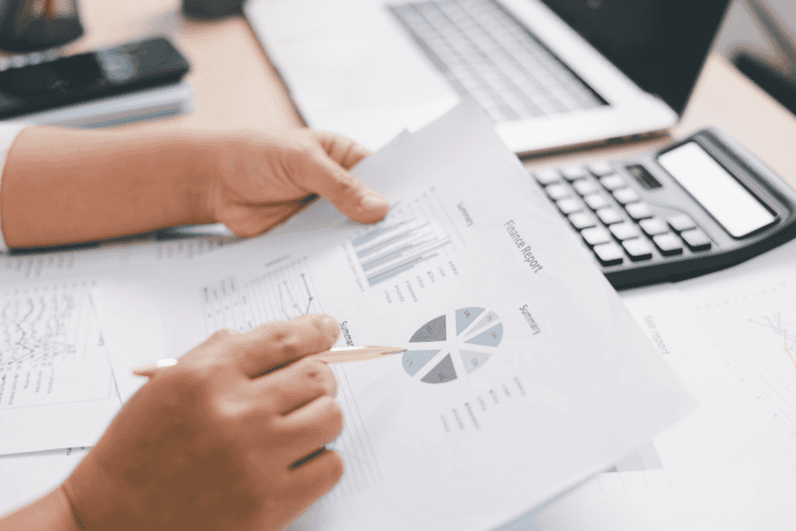 Hands reviewing a financial report with charts beside a laptop and calculator for weekly budget tracking