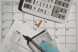 Calculator, cash, credit card, and tax form on a calendar for a weekly budget review routine